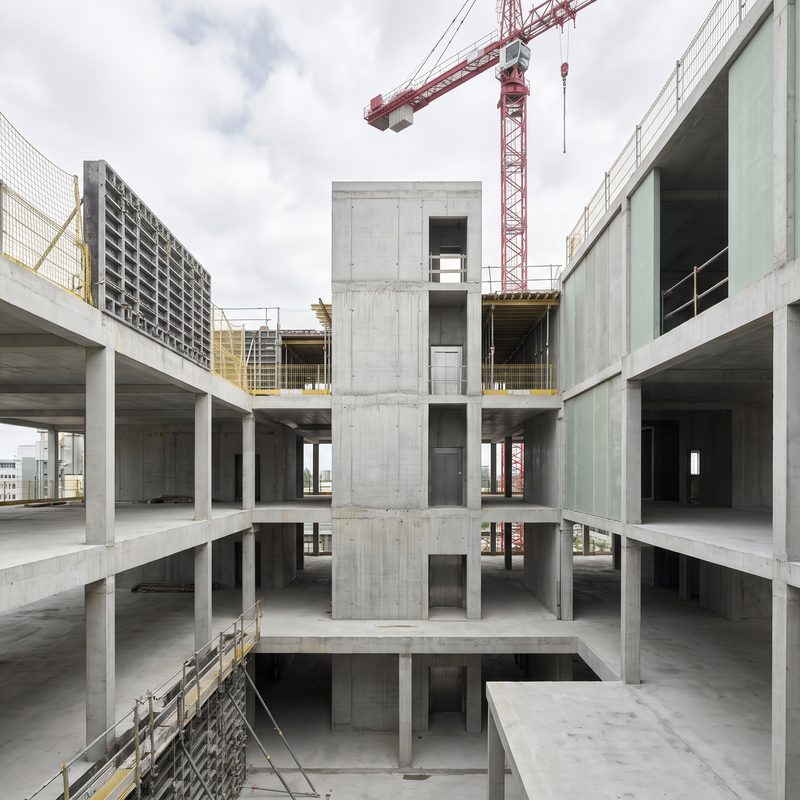 Exposed cast-concrete structural frame of a building under construction beneath a tower crane
